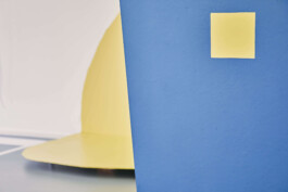 An art installation by Eva Funk with large abstract shapes in red, yellow, blue, and purple, displayed in an industrial-style gallery space. White walls and geometric patterns on the floor. Artist  Eva Funk