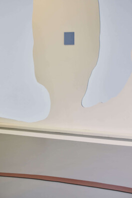 An art installation by Eva Funk with large abstract shapes in red, yellow, blue, and purple, displayed in an industrial-style gallery space. White walls and geometric patterns on the floor. Artist  Eva Funk