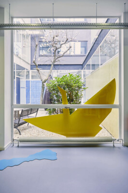 An art installation by Eva Funk with large abstract shapes in red, yellow, blue, and purple, displayed in an industrial-style gallery space. White walls and geometric patterns on the floor. Artist  Eva Funk