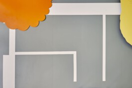 An art installation by Eva Funk with large abstract shapes in red, yellow, blue, and purple, displayed in an industrial-style gallery space. White walls and geometric patterns on the floor. Artist  Eva Funk